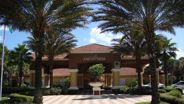Entrada de hotel con techo de tejas rojas, palmeras y un camino a cuadros que lleva a la entrada.