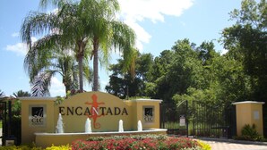 Letrero de Encantada con un logotipo de lagarto, rodeado por un jardín ajardinado con diversas plantas y una entrada con portón.