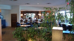 Un comedor interior con mesas, sillas, una barra y plantas en macetas.