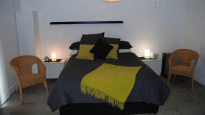 Un dormitorio con cama, mesitas de noche y dos sillas de mimbre.