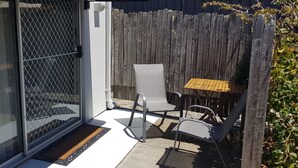 Un patio con puerta corrediza de vidrio, una mesa pequeña, dos sillas y una valla de madera.