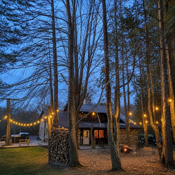 A rustic cabin surrounded by tall trees, with string lights and a fire pit visible. - Brech Mountain House-Hudson Valley (Pine Bush)