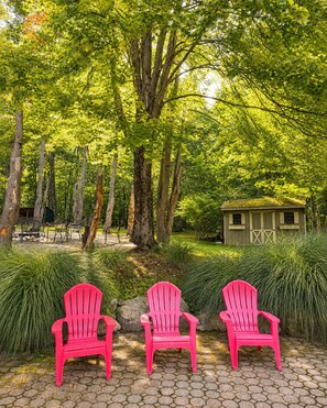 A garden with three red chairs, a wooden structure, and a tree-lined path.