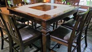 Een eetgedeelte met een grote houten tafel, omringd door stoelen, een spiegel aan de muur en uitzicht op groen buiten.