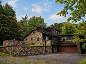 A two-story stone house with a garage, surrounded by trees.