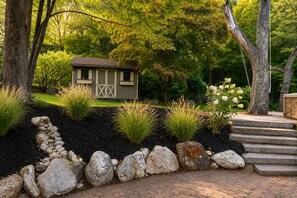 A garden with a small shed, stone pathway, and steps leading to a wooden deck. - Brech Mountain House-Hudson Valley (Pine Bush)
