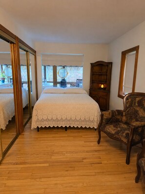 A bedroom with a large bed, a chair, a wooden cabinet, and a mirror.