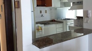 A modern kitchen with white cabinets, a granite countertop, and a stove. - Apartment with ocean view. 2 bedrooms. BORACEIA BEACH (boraceia)