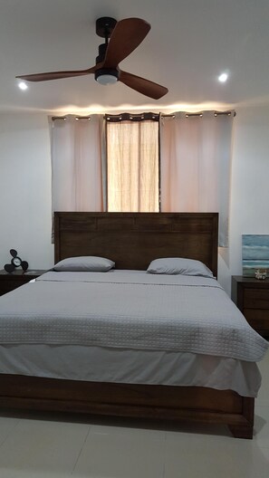 Relax in this serene bedroom with a large bed, ceiling fan, and a nightstand with a clock.