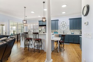 Modern kitchen and dining area with a central island and round window, featuring a white table and leather sofa.