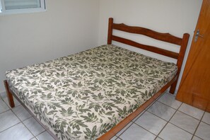 A single bed with a wooden frame and a floral-patterned mattress in a room with tiled flooring and a wooden door.