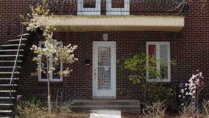 A two-story brick building with a white front door, two windows on the upper floor, and a small balcony with a metal railing. - Lovely and quiet location near the Botanical Garden, 15 min downtown. (Montréal)