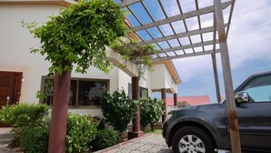 Ein Auto vor einem Haus mit einer Pergola, einem Fenster und einem gepflasterten Weg.