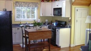 Une cuisine de taille réduite avec des meubles blancs, une cuisinière et une fenêtre agrémentée de rideaux.