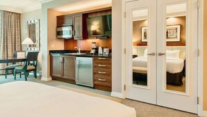 A hotel room with a bed, a kitchenette with a microwave, and a dining area with a table and chairs.