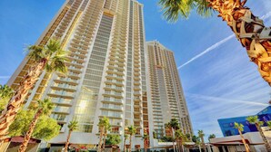 A high-rise hotel with multiple balconies, palm trees, and a clear sky.