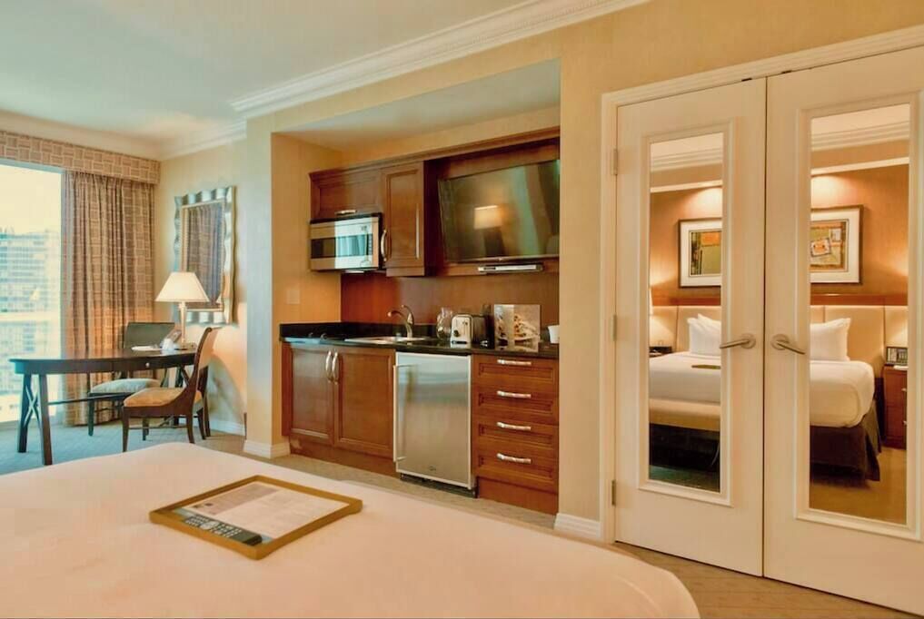 A hotel room with a kitchenette, a dining area, a bed, and a view of the city.