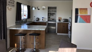 A modern kitchen with a marble countertop, two bar stools, a built-in oven, and a refrigerator. - Serenity - our home away from home (Whitianga)