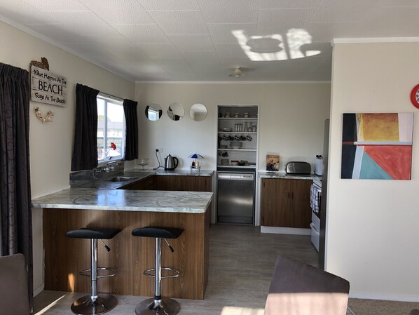 A modern kitchen with a marble countertop, two bar stools, a built-in oven, and a refrigerator.