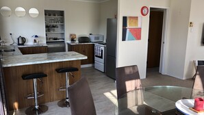 A modern kitchen with a marble countertop, wooden bar stools, and a glass dining table. - Serenity - our home away from home (Whitianga)