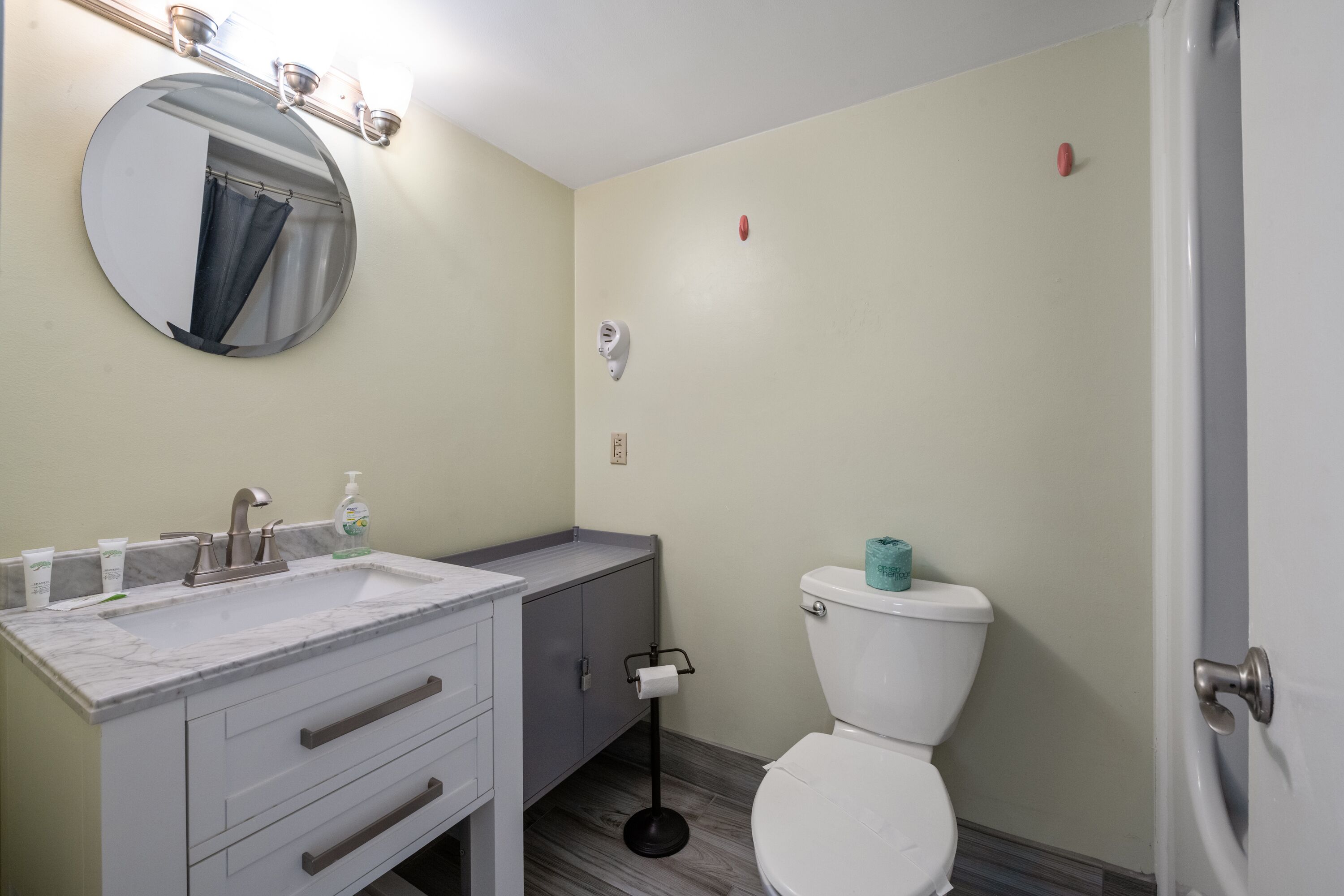 A bathroom with a white sink, mirror, and toilet, marble countertop, and a towel rack.