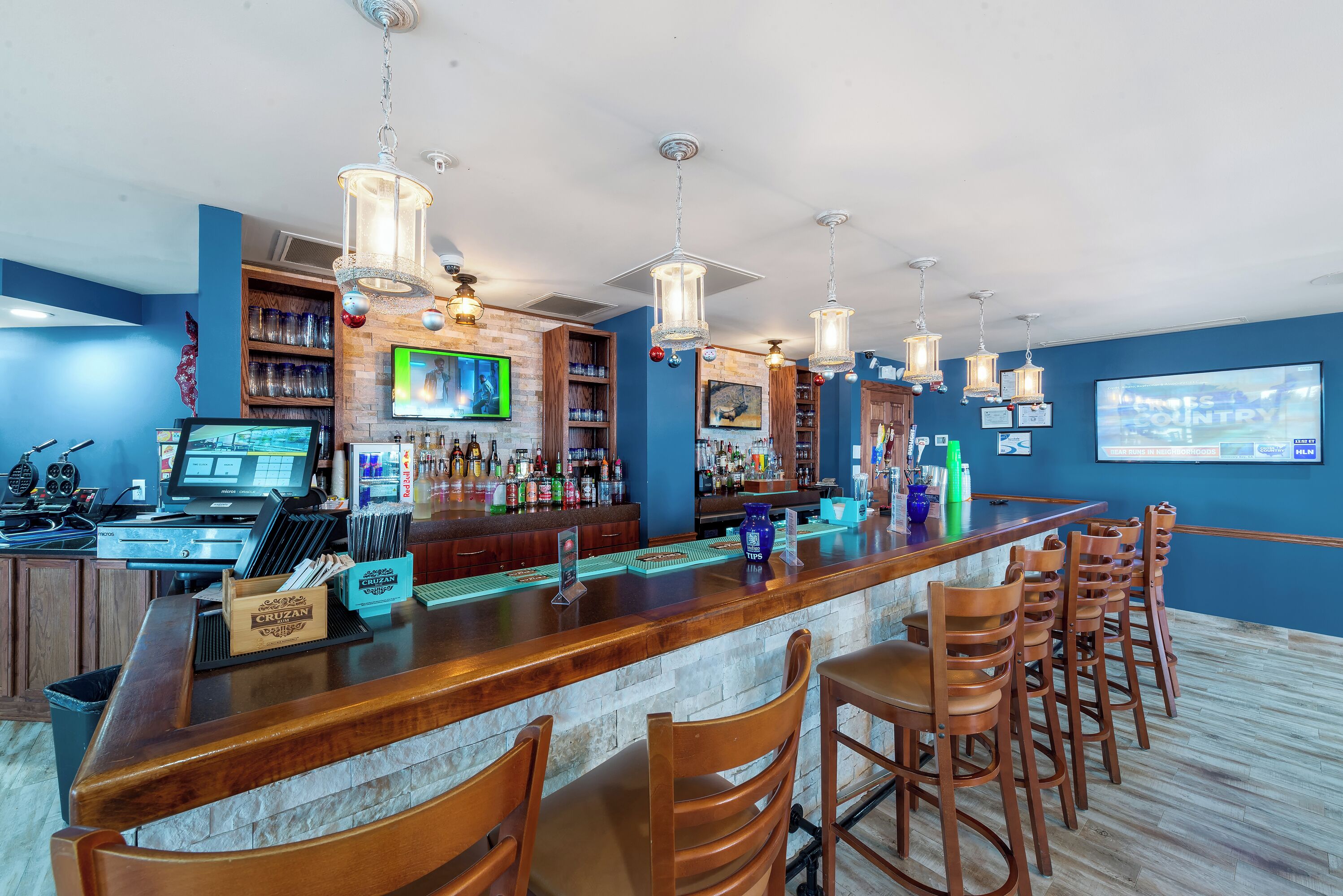 A bar area with a long counter, multiple hanging lights, and a television screen.