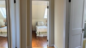 A hallway leading to a bedroom with a bed, wooden flooring, and a window. - Oceanfront Cape with dock on Bass Harbor (Bernard)