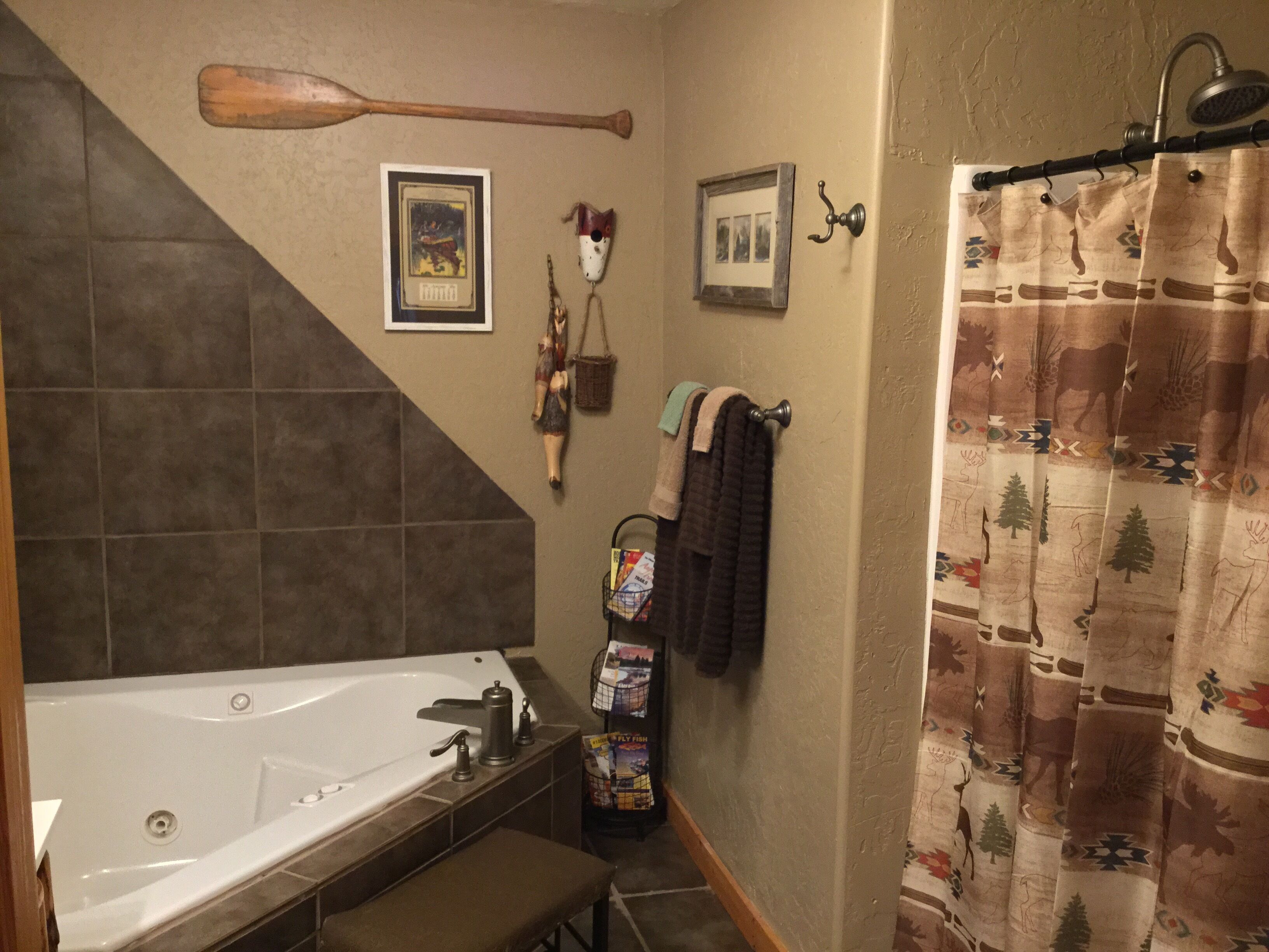 A bathroom with a bathtub, a shower curtain with a nature print, a wooden bat hanging on the wall, and a framed picture.