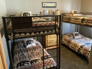 Cozy dormitory room with bunk beds and a dresser, featuring patterned bedding and a framed picture on the wall.