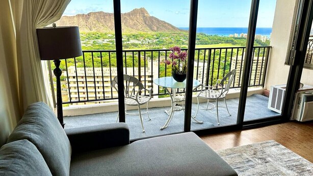 Un balcon avec vue sur les montagnes et la mer, un canapé, une table avec des chaises et une lampe.