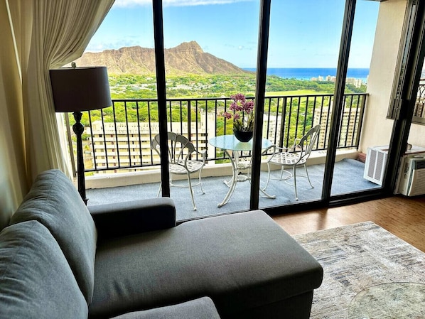 Ein Balkon mit Blick auf Berge und Meer, eine Couch, ein Tisch mit Stühlen und eine Lampe.