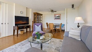 Un salon comprenant un téléviseur, un canapé, une table à manger, des chaises et un ventilateur de plafond.