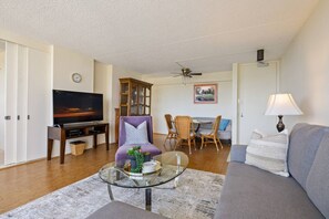 A living room with a TV, sofa, dining table, chairs, and a ceiling fan.