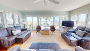 A spacious living room with a large TV, two leather sofas, a coffee table, and a view of the beach through large windows. - Spacious, Luxe Design, Large Balcony & Incredible Views! (Tybee Island)