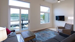 Ein geräumiges Wohnzimmer mit großem Fenster mit Blick auf ein Gewässer, einem Deckenventilator und einem flachbildfernseher an der Wand.