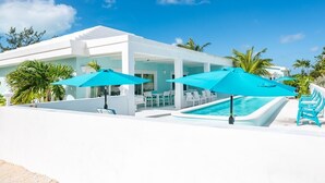 A modern poolside area with a pool, white lounge chairs, and blue umbrellas. - Aqua Dreams, Htd Priv Salt Pool, At Beach, Guest hse, 4 Kng BRs for 12, Lg Spa!! (Georgetown)