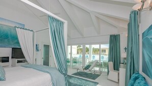 A modern bedroom with a large bed, a TV, and a view of an outdoor pool area. - Aqua Dreams, Htd Priv Salt Pool, At Beach, Guest hse, 4 Kng BRs for 12, Lg Spa!! (Georgetown)