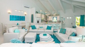 A spacious living area with white furniture, teal accents, and a kitchen in the background. - Aqua Dreams, Htd Priv Salt Pool, At Beach, Guest hse, 4 Kng BRs for 12, Lg Spa!! (Georgetown)