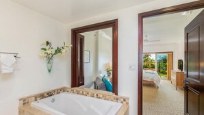 Une salle de bain moderne avec une grande baignoire, un miroir et une vue sur une chambre à coucher équipée d’un lit et d’un téléviseur.