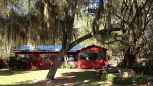 A red house with a covered porch, surrounded by trees with hanging moss. - Island Lake Redwood Cottage With Canoe and Grill:  Relax, Swim, Fish, Ski, Enjoy (Fort McCoy)