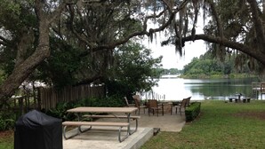 An outdoor patio area with picnic tables and chairs, a covered grill, and a view of a lake. - Island Lake Redwood Cottage With Canoe and Grill:  Relax, Swim, Fish, Ski, Enjoy (Fort McCoy)
