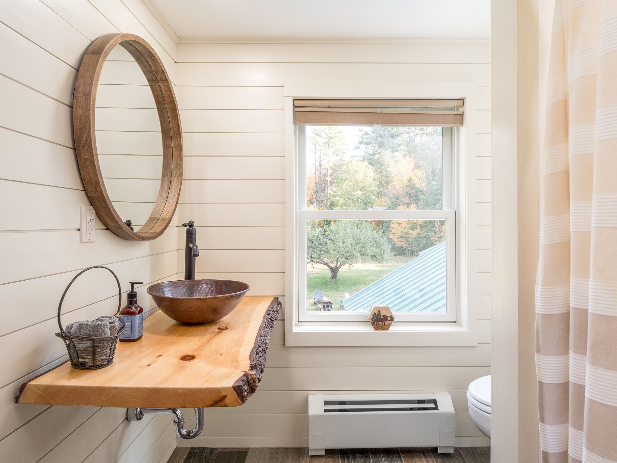 A bathroom with a wooden vanity, a large mirror, a window with a view of trees, and a radiator.