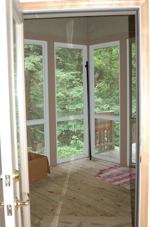 Una habitación con terraza de madera, ventanas amplias y vista al bosque.