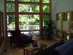 Una sala de estar con ventanas amplias, una mesa de madera, una silla y una lámpara.