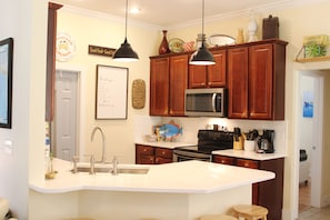 A kitchen with wooden cabinets, a white countertop, a stainless steel microwave, and a sink.
