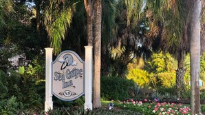 A sign for Sea Grapes Inn with a bird illustration, surrounded by a garden with pink and white flowers. - Sea Grape Inn #3 - Beachfront Property (Longboat Key)