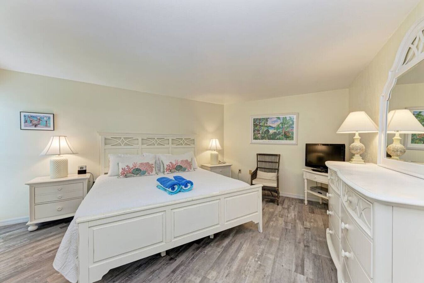 A hotel room with a large bed, two bedside tables with lamps, a chair, a TV, and a dresser.