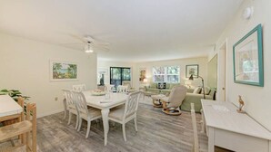 A spacious living room with a dining area, a ceiling fan, and a large window providing natural light. - Sea Grape Inn #3 - Beachfront Property (Longboat Key)
