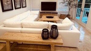 Een moderne woonkamer met een witte hoekbank, een houten salontafel en twee zwarte kandelaars.