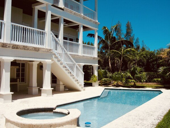 A two-story building with a pool and hot tub, surrounded by palm trees.